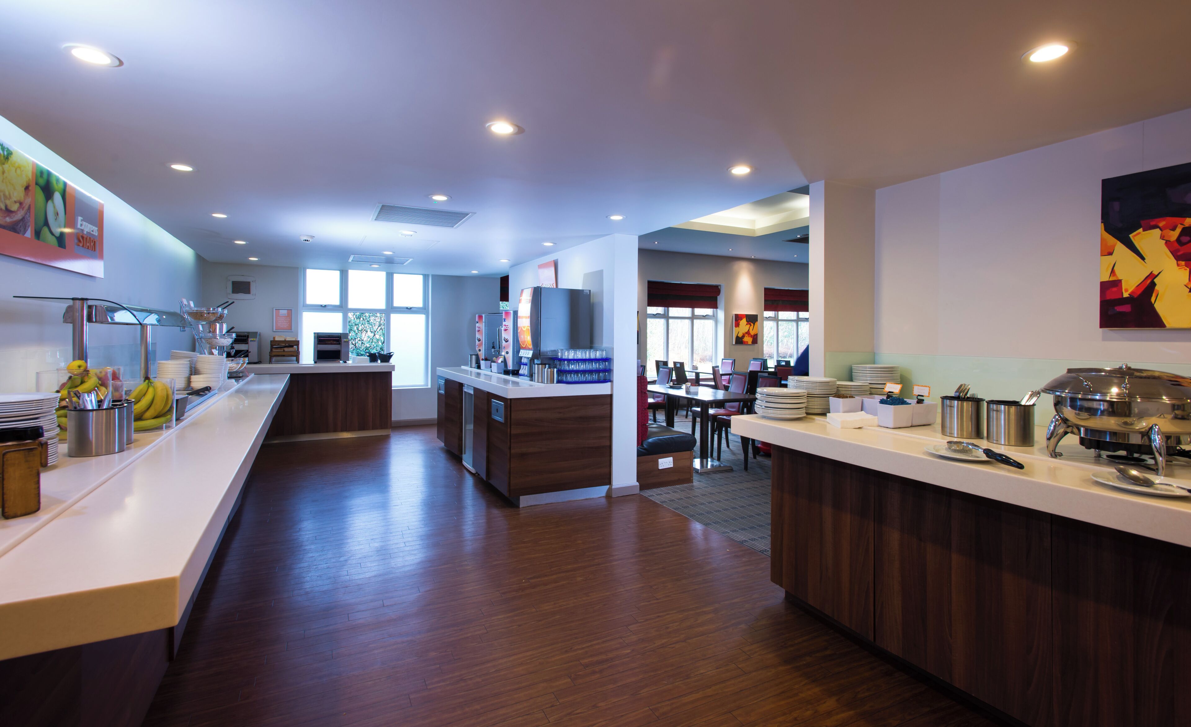 A modern hotel kitchen with a central island, a dining area, and a view of the outdoors.