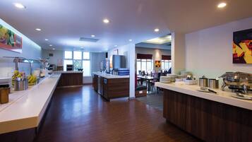 A modern hotel kitchen with a central island, a dining area, and a view of the outdoors.