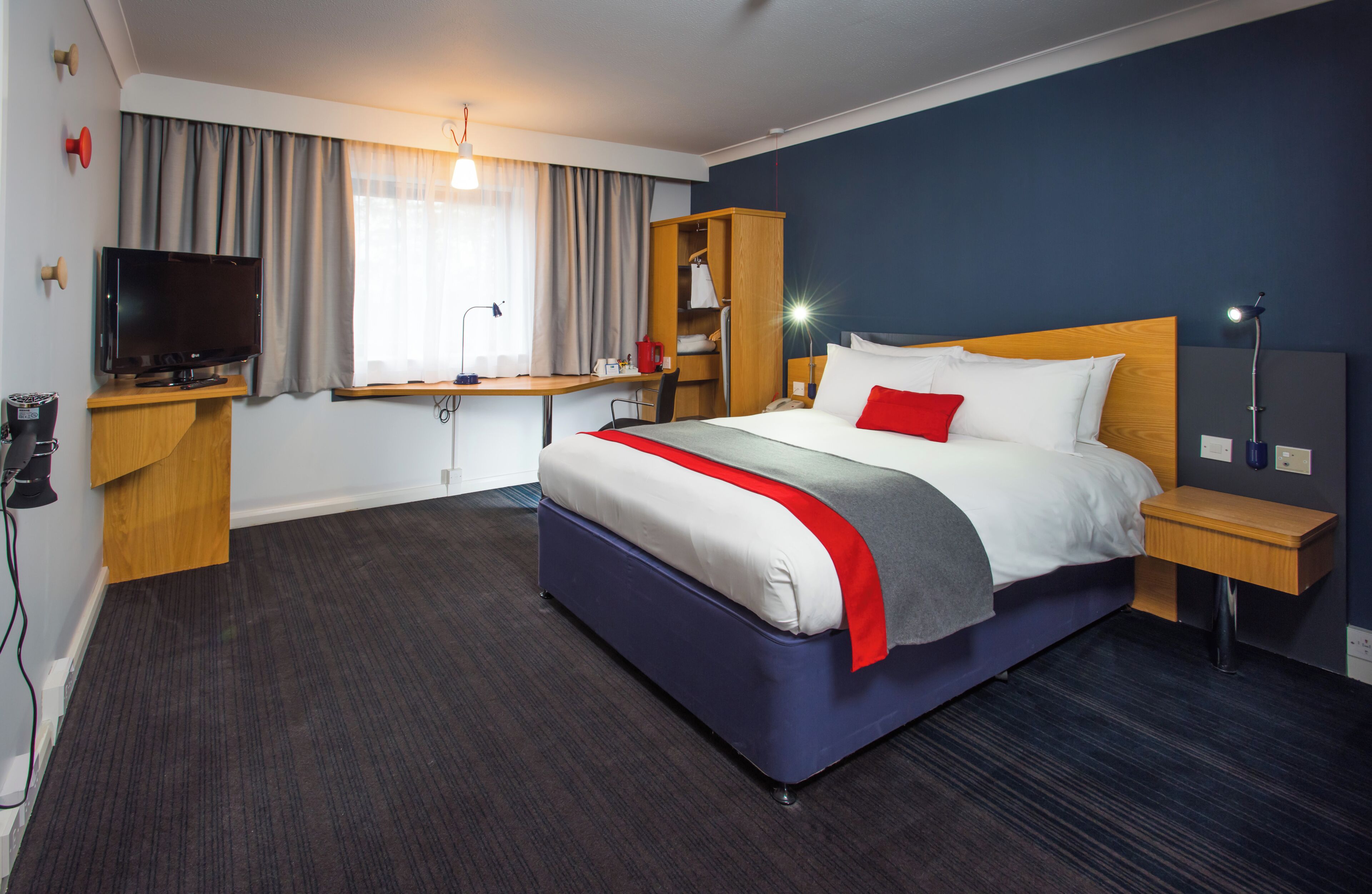 A hotel room with a bed, a desk, a television, a wardrobe, and a nightstand.