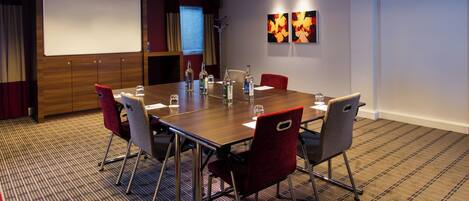 A conference room with a wooden table, red and grey chairs, a projector screen, and abstract wall art.