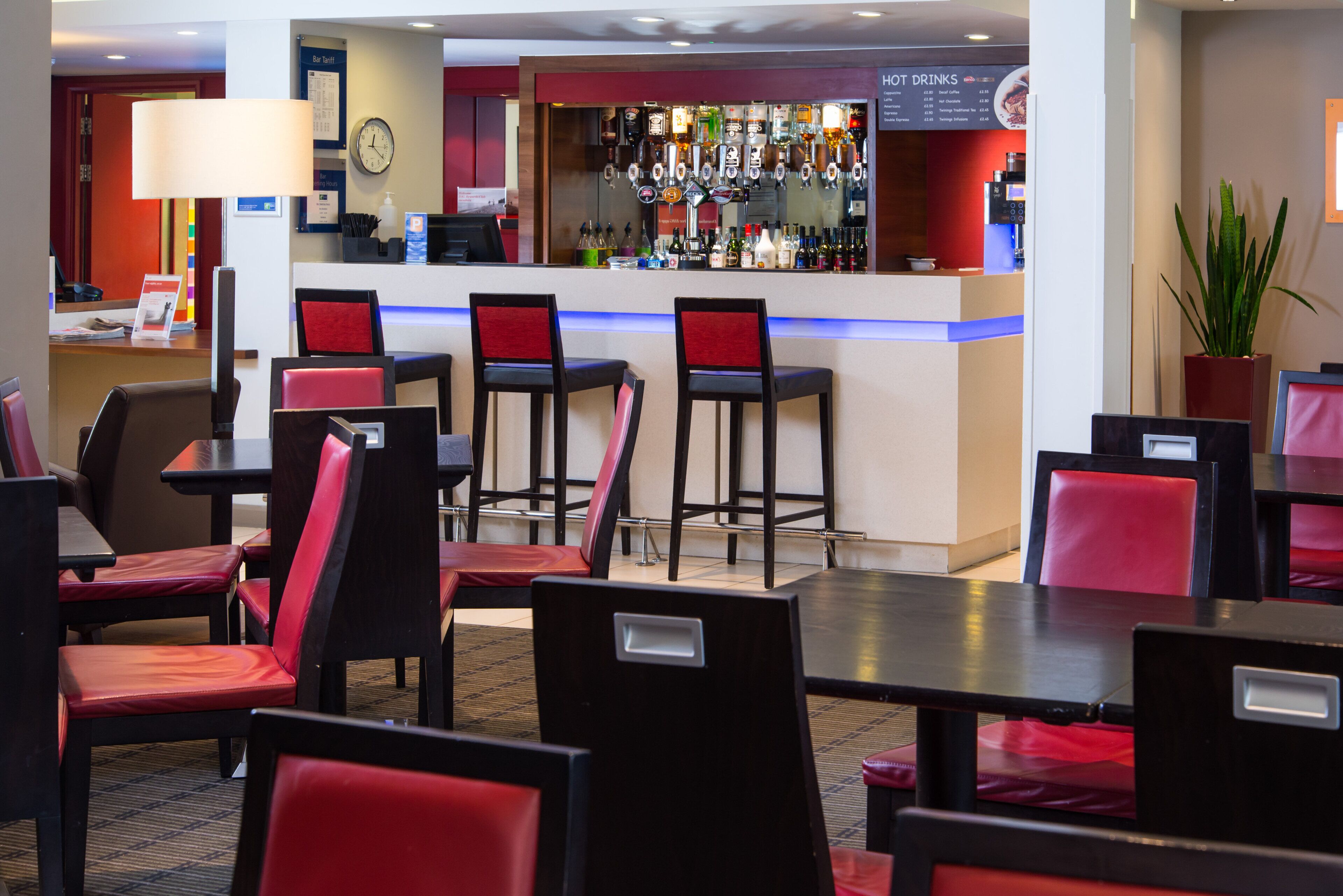 A hotel lobby with a bar area, multiple seating arrangements, and a clock on the wall.