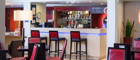 A hotel lobby with a bar area, multiple seating arrangements, and a clock on the wall.