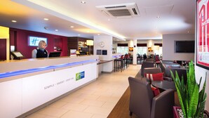 A hotel reception area with a counter, a clock, and a seating area with tables and chairs. - Holiday Inn Express Stoke On Trent by IHG (Stoke-on-Trent)