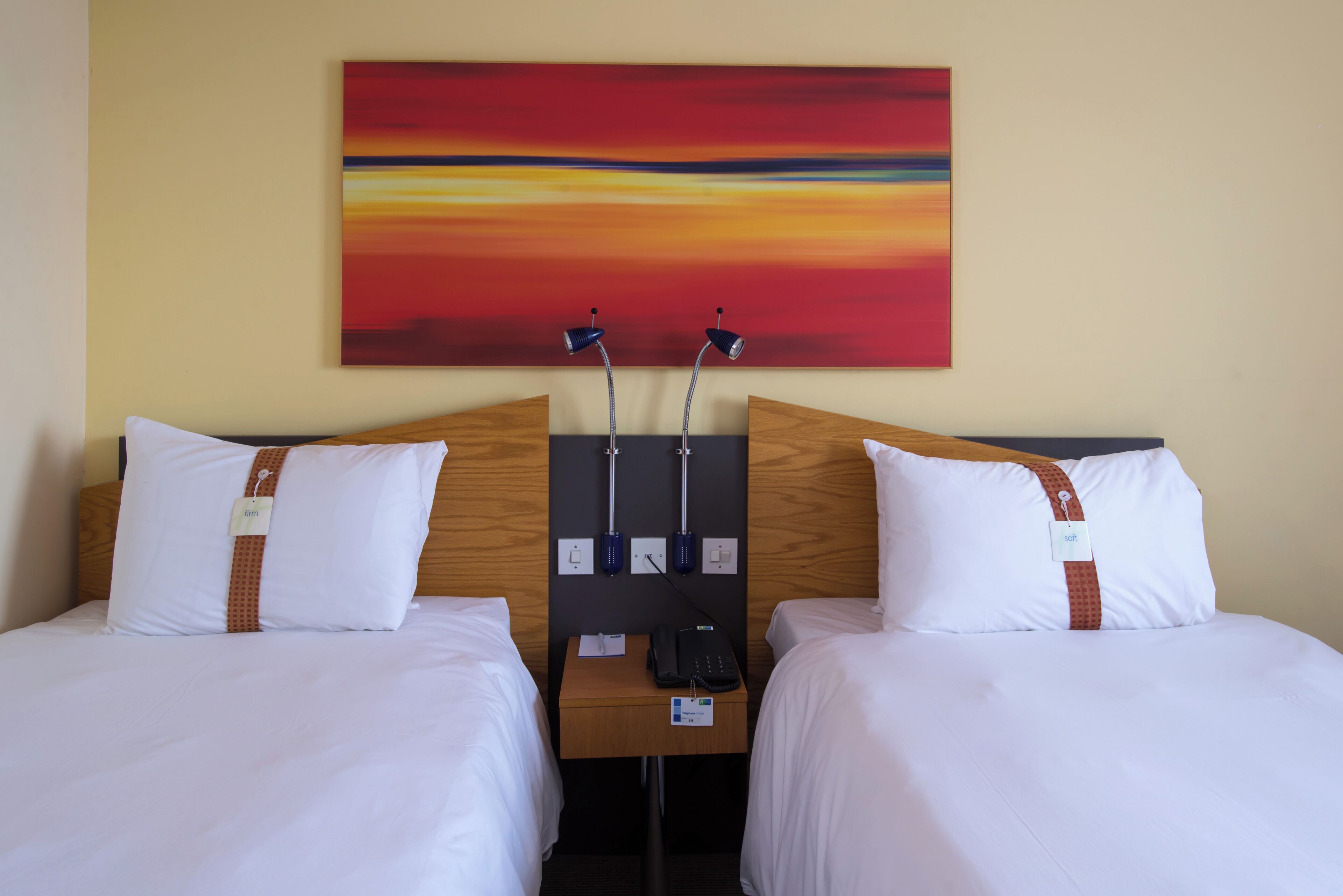 Ein Hotelzimmer mit zwei Betten, einem hölzernen Kopfteil, einem Nachttisch mit Telefon und einem Bild an der Wand.