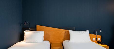 A hotel room with two single beds, wooden headboards, white bedding, and bedside lamps.