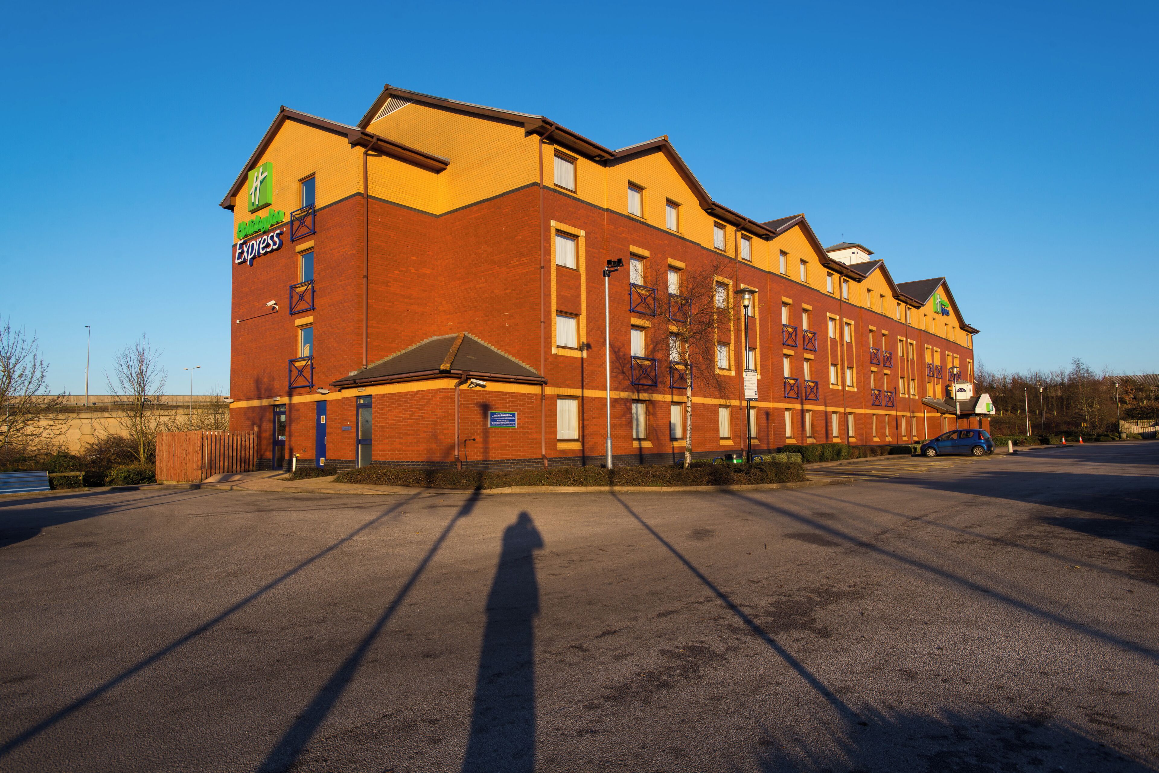 Un edificio de ladrillo grande con un letrero de Holiday Inn Express, múltiples ventanas y un estacionamiento.