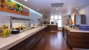 A modern kitchen with a long counter, a fruit display, and a refrigerator. - Holiday Inn Express Stoke On Trent by IHG (Stoke-on-Trent)