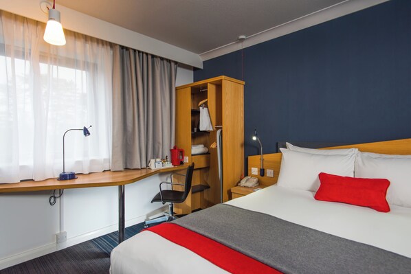 A hotel room with a bed, a desk with a chair, a wardrobe, and a window with curtains. - Holiday Inn Express Stoke On Trent by IHG (Stoke-on-Trent)