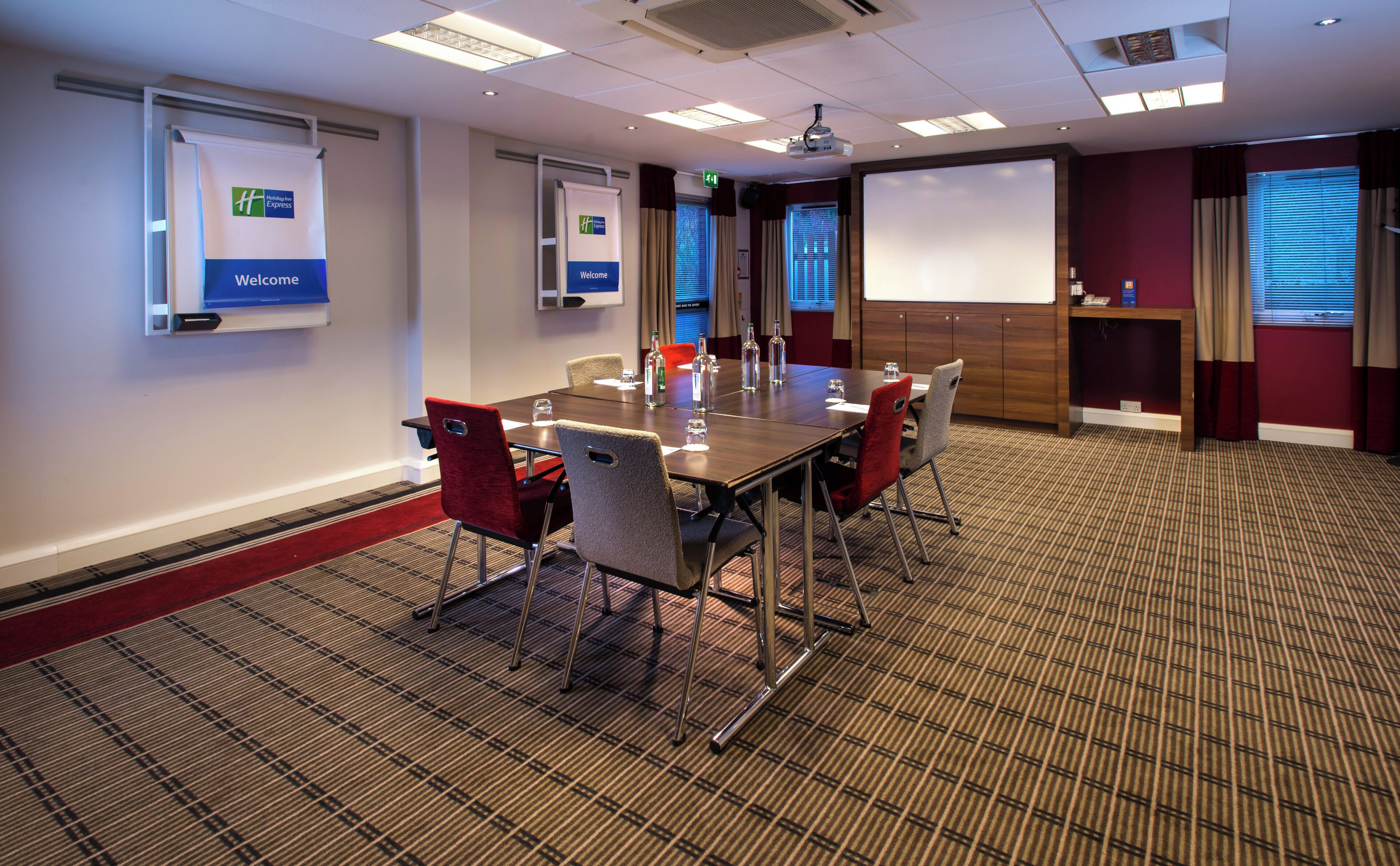 A conference room with a large table, chairs, a projector screen, and a 'Welcome' sign.