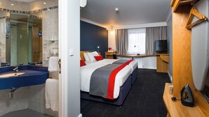 A hotel room with a large bed, a desk, a television, a mirror, and a bathroom with a sink and shower. - Holiday Inn Express Stoke On Trent by IHG (Stoke-on-Trent)