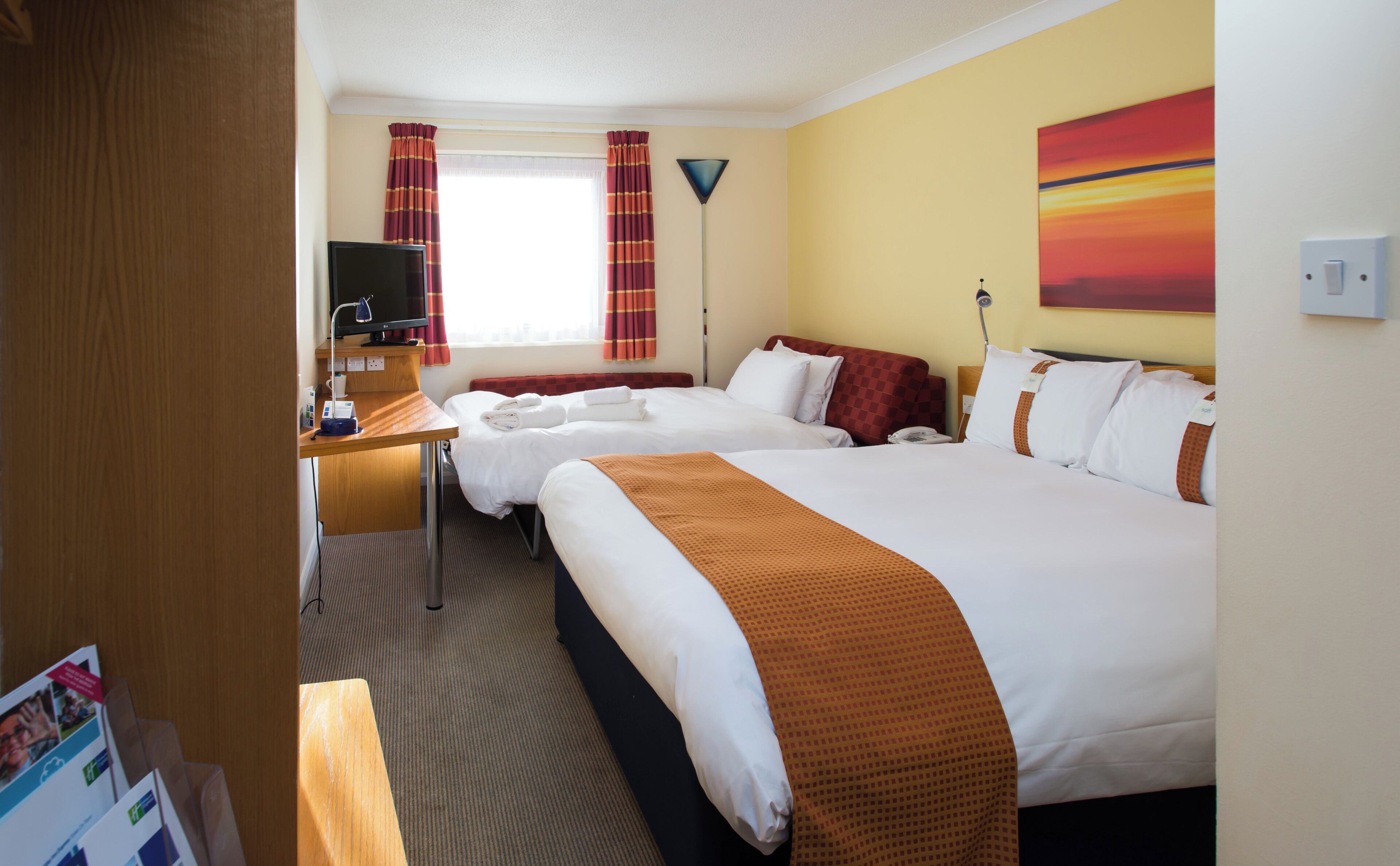 Een hotelkamer met twee bedden, een bureau, een televisie, een telefoon en een schilderij aan de muur.