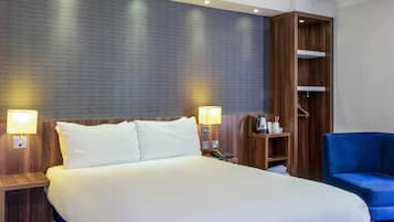 Una habitación de hotel con una cama grande, dos lámparas de noche, un armario de madera y un sillón azul.