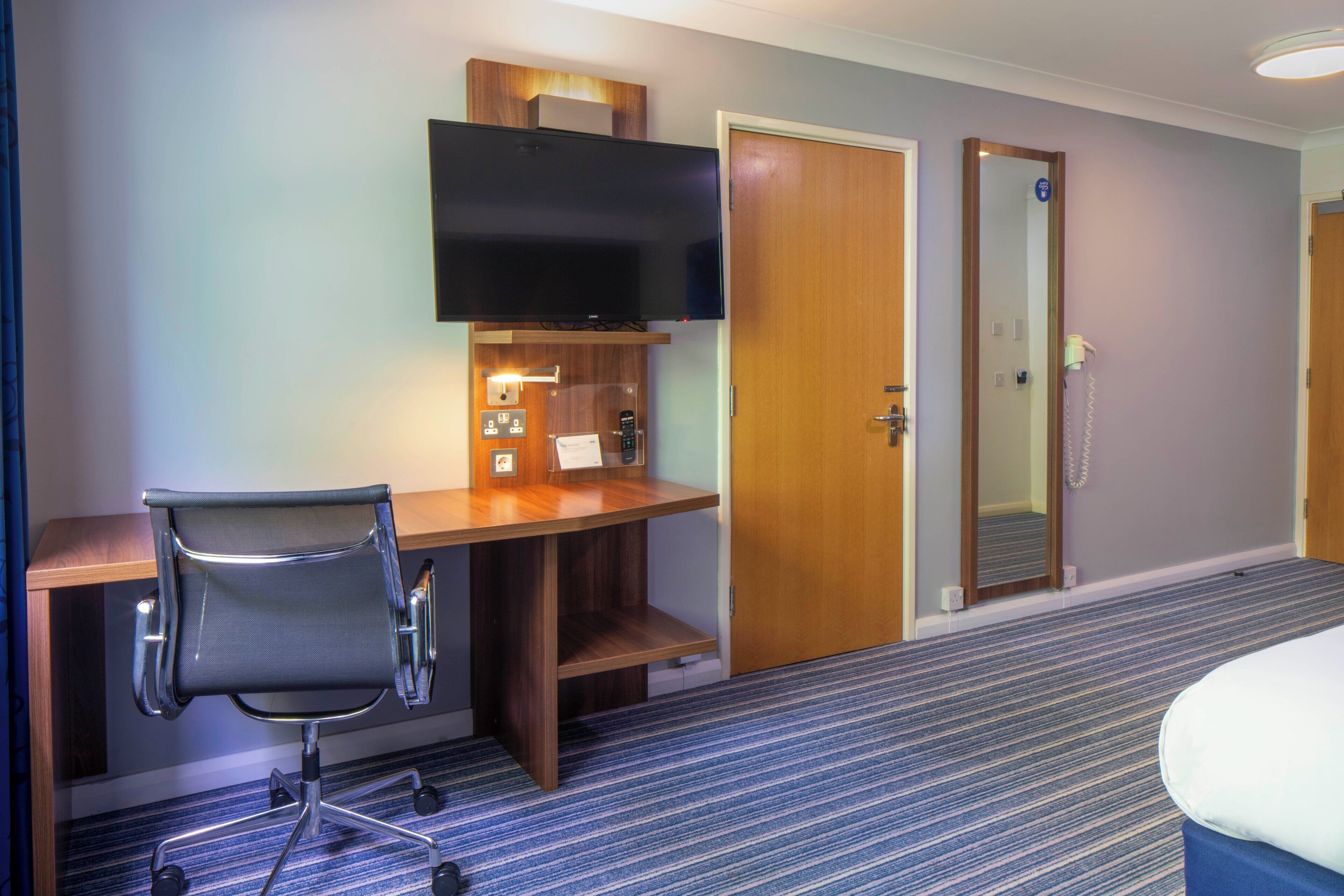 Een hotelkamer met een bureau, stoel, televisie en een deur.
