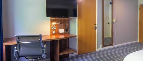 Een hotelkamer met een bureau, stoel, televisie en een deur.