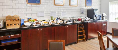 A breakfast bar with various food options, wooden cabinets, and a seating area with tables and chairs.