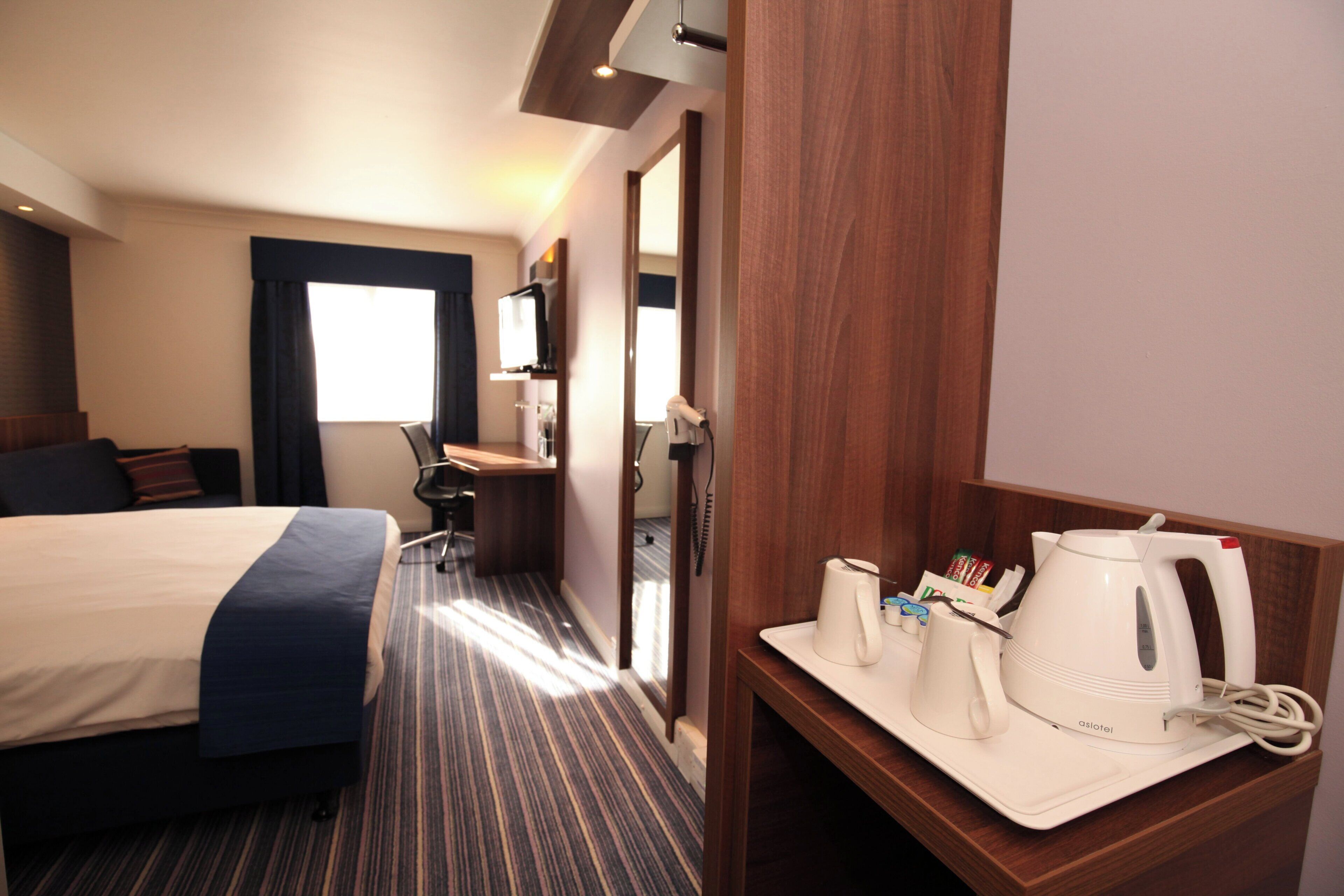 A hotel room with a bed, a desk, a coffee maker, and a telephone.