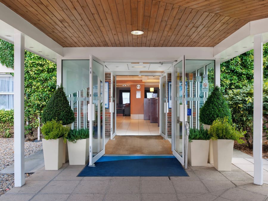 Una entrada moderna con puertas de vidrio, techo de madera y una alfombra azul que conduce a un espacio interior.