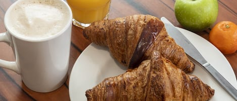 A plate with croissants, a glass of orange juice, an apple, and an orange.