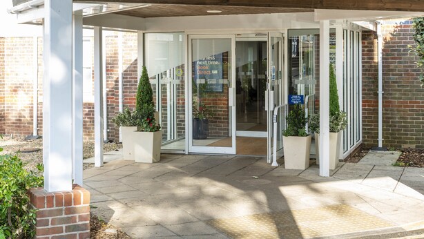 A building entrance with glass doors, a brick wall, and potted plants.
