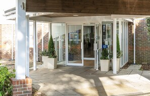 A building entrance with glass doors, a brick wall, and potted plants. - Holiday Inn Express York by IHG (York)