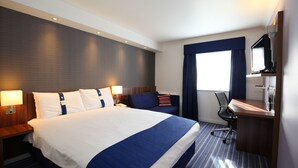 A hotel room with a large bed, a desk with a computer, a chair, and a TV.