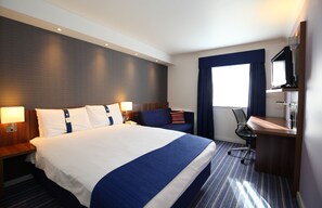 A hotel room with a large bed, a desk with a computer, a chair, and a TV.