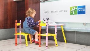 A child sitting at a table with crayons, in front of a wall with the Holiday Inn Express logo. - Holiday Inn Express York by IHG (York)