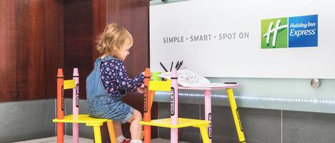 A child sitting at a table with crayons, in front of a wall with the Holiday Inn Express logo.