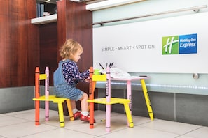 A child sitting at a table with crayons, in front of a wall with the Holiday Inn Express logo. - Holiday Inn Express York by IHG (York)