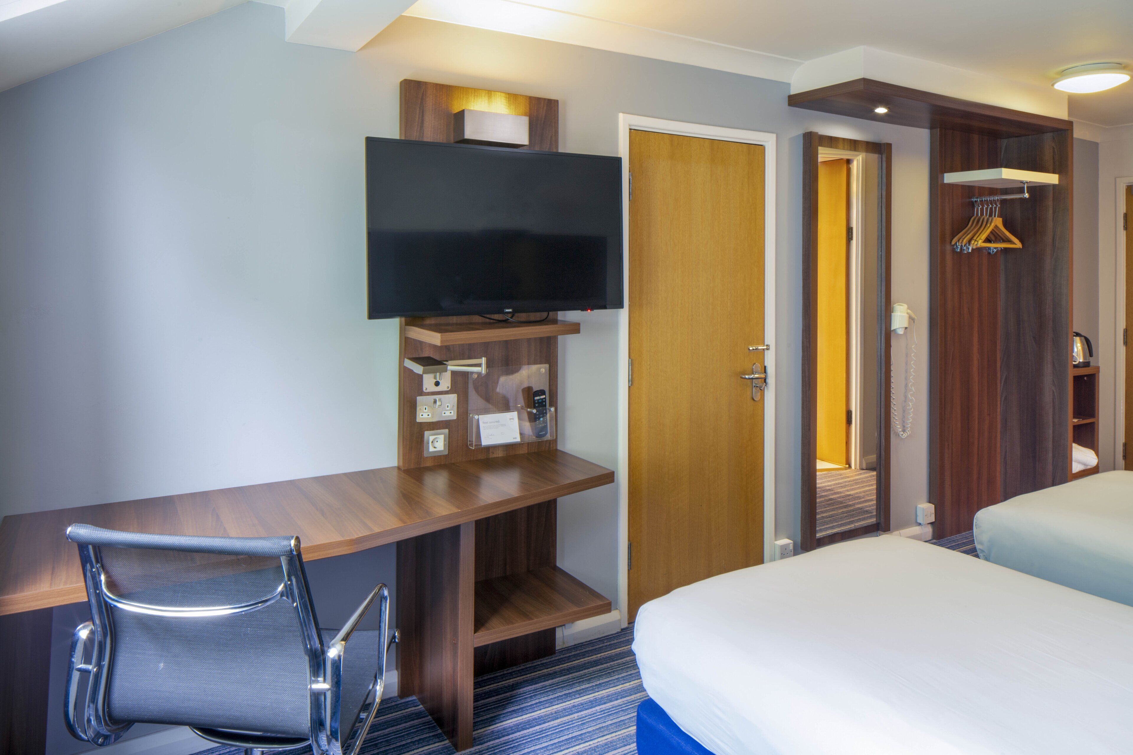 Ett hotellrum med en säng, ett skrivbord med en stol, en tv och en garderob.