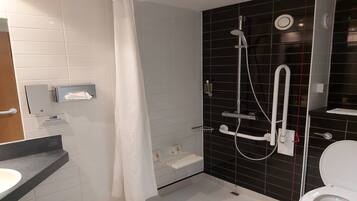 A modern bathroom with a shower, toilet, and a towel dispenser.