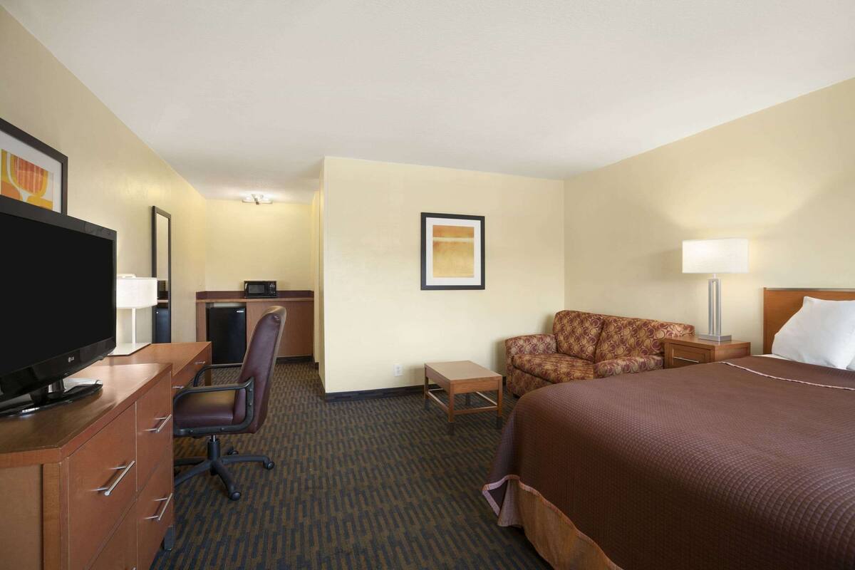 A hotel room with a bed, a desk with a computer, a chair, a television, and a lamp.