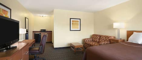 A hotel room with a bed, a desk with a computer, a chair, a television, and a lamp.