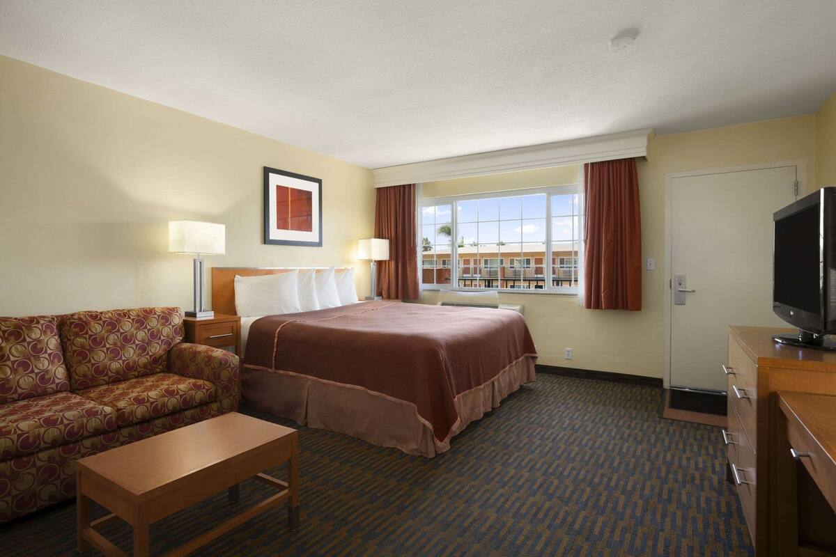 A hotel room with a bed, a sofa, a desk, a TV, and a window with curtains.