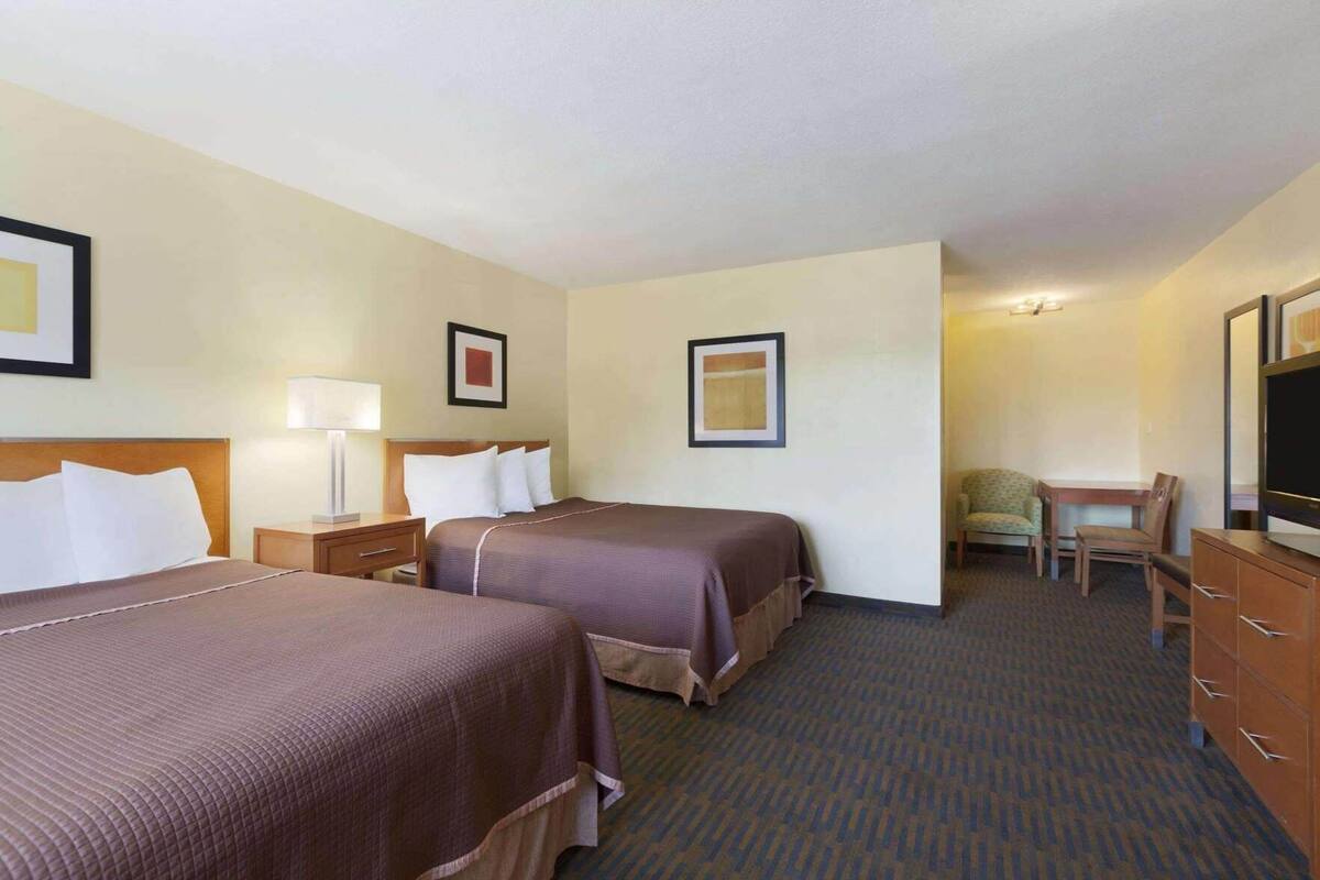 A hotel room with two beds, a desk, a chair, a television, and a lamp.