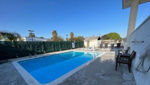 A rectangular swimming pool with a blue interior, surrounded by a concrete deck. There are lounge chairs and a small building in the background. - Vivo Hotel (Stanton)