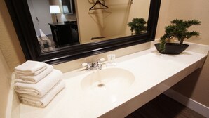 Un bagno con lavandino, specchio, pila di asciugamani e un bonsai.