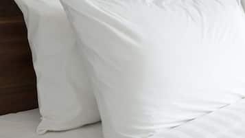 Uma cama com roupa de cama branca e almofada listrada.