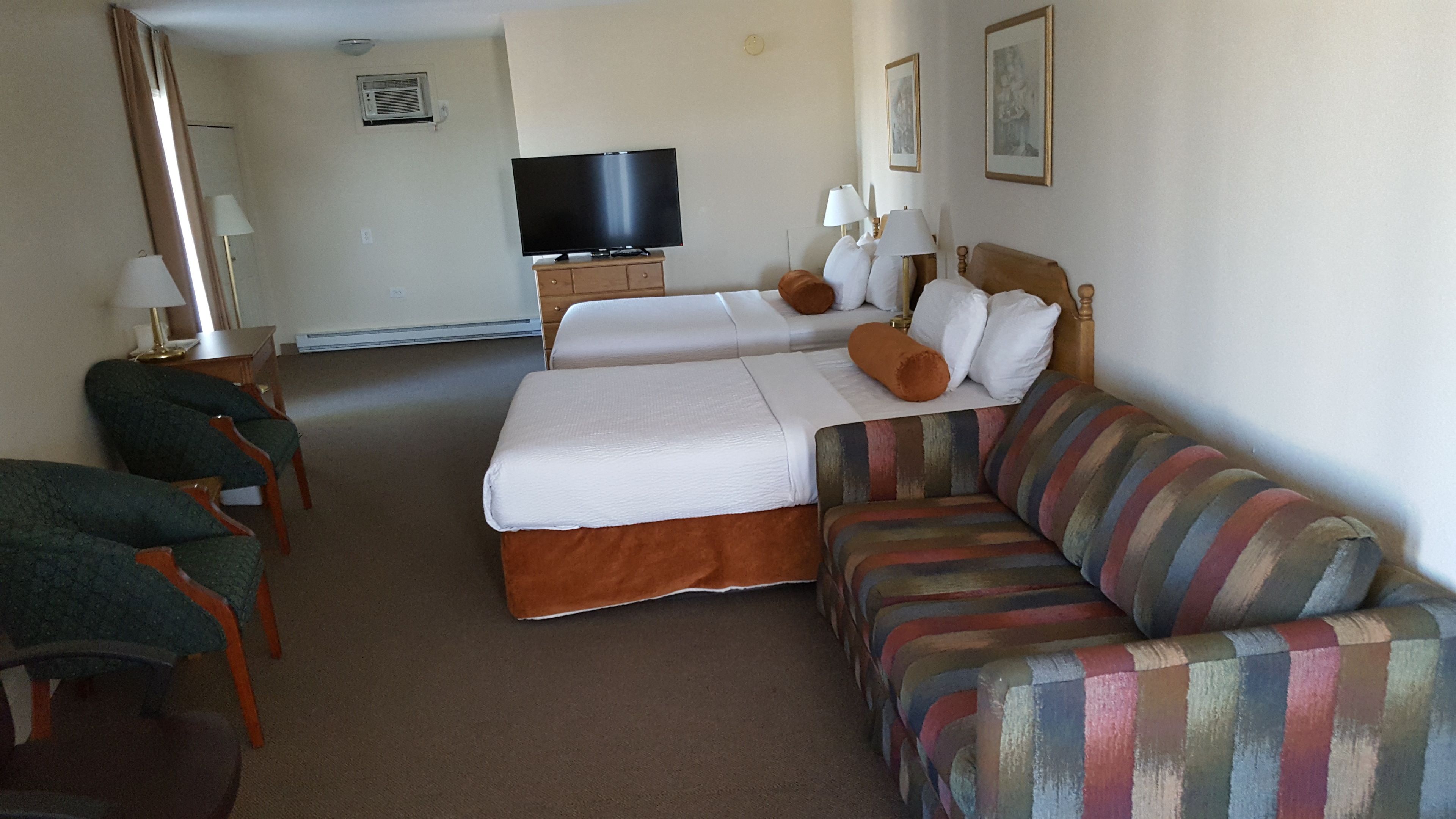 A hotel room with two beds, a television, a sofa, and a desk with a lamp.