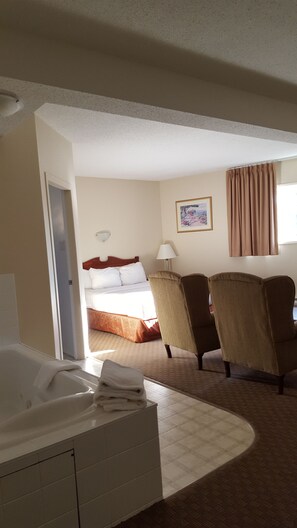 A hotel room with a bed, two armchairs, a desk, a window with curtains, and a painting on the wall. - Knights Inn Lethbridge (Lethbridge)