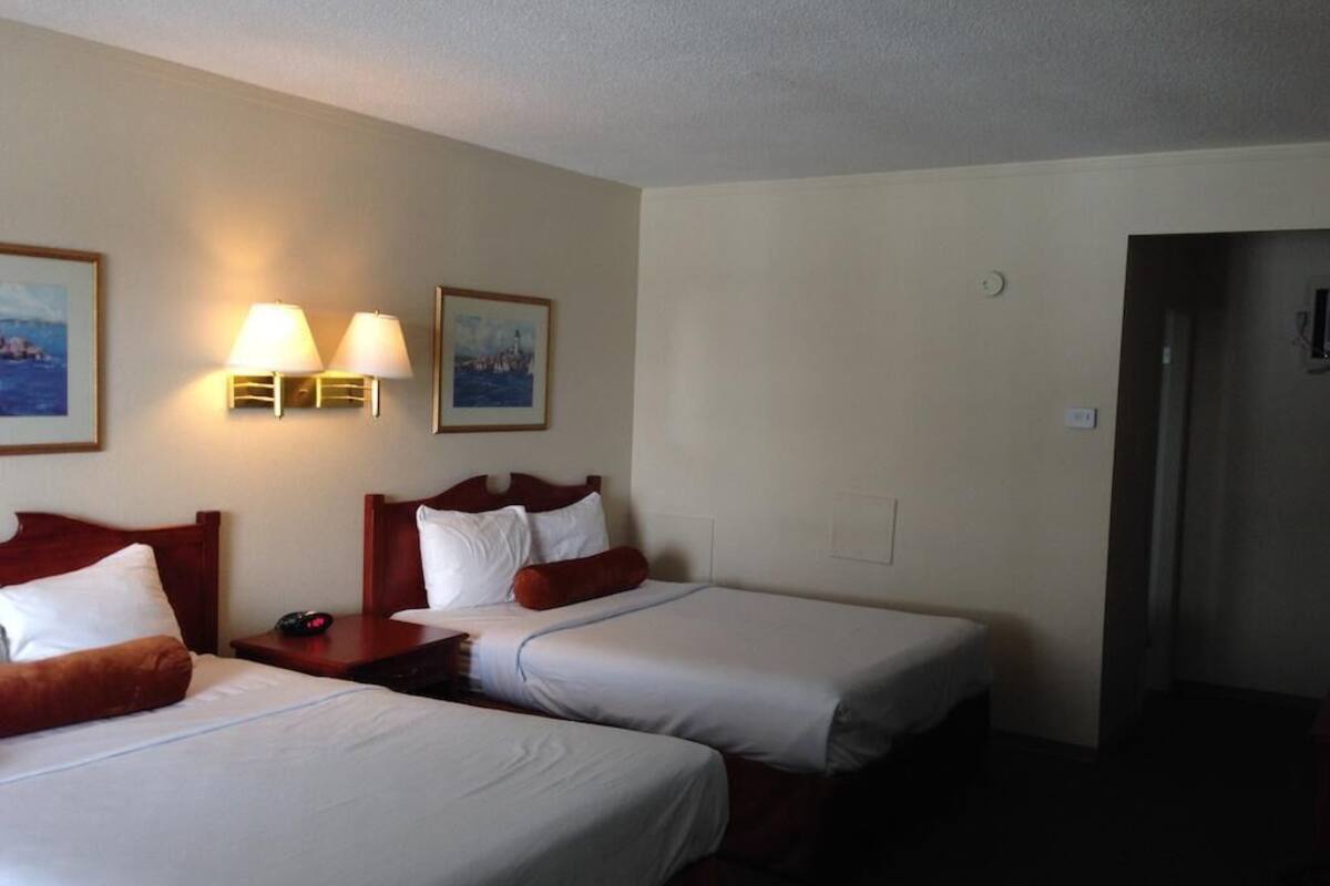 A hotel room with two beds, bedside lamps, and framed pictures on the wall.