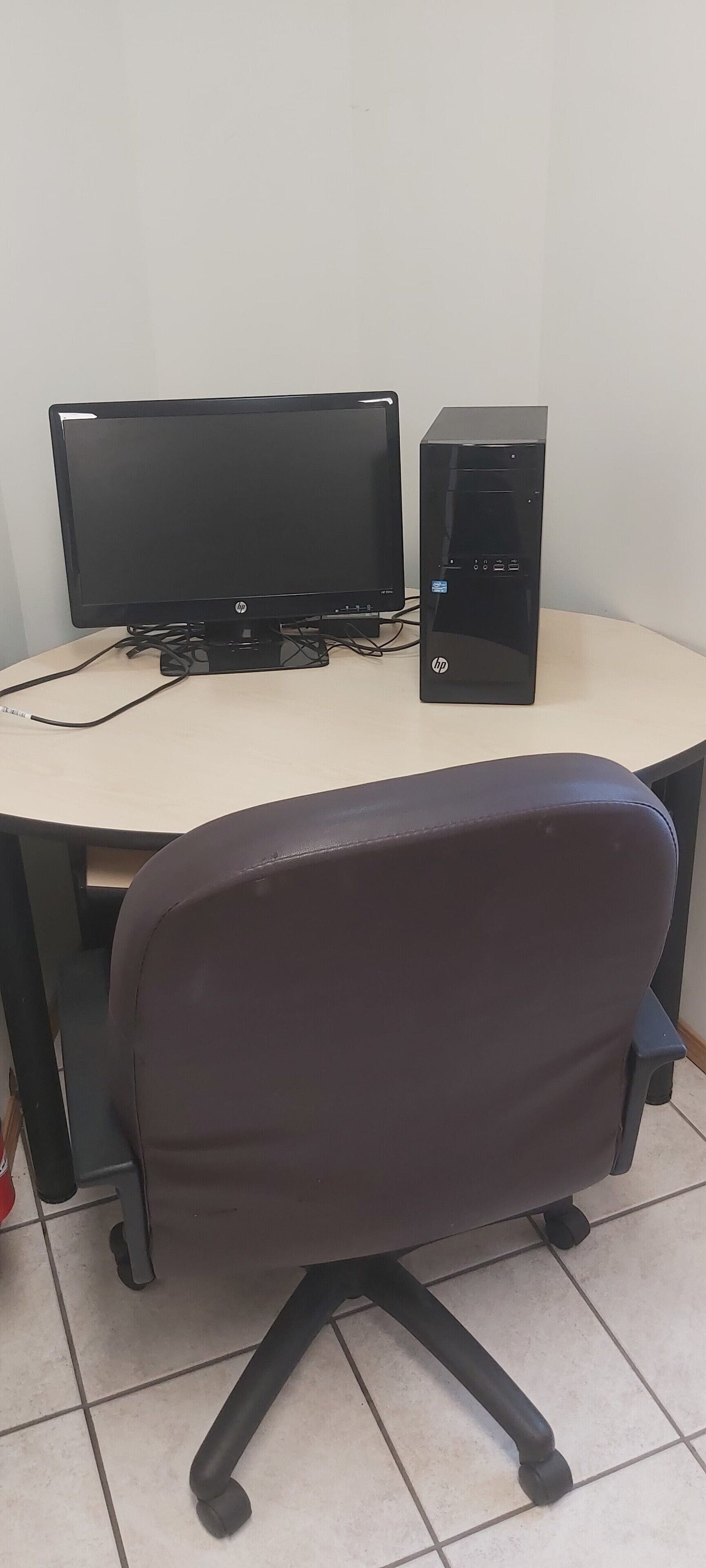 Et skrivebord med en computeropsætning, inklusiv en skærm og en PC, samt en sort kontorstol.