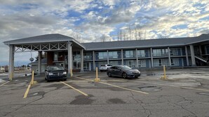 A parking lot with two cars, a building with a flat roof, and a clear sky with clouds. - Knights Inn Lethbridge (Lethbridge)
