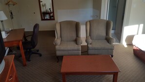 A hotel room with two armchairs, a wooden table, a desk with a chair, a bed, and a mirror on the wall. - Knights Inn Lethbridge (Lethbridge)
