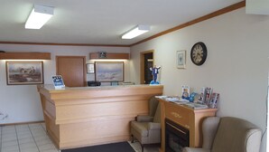 A reception area with a wooden desk, framed artwork, a clock, and a fireplace. - Knights Inn Lethbridge (Lethbridge)