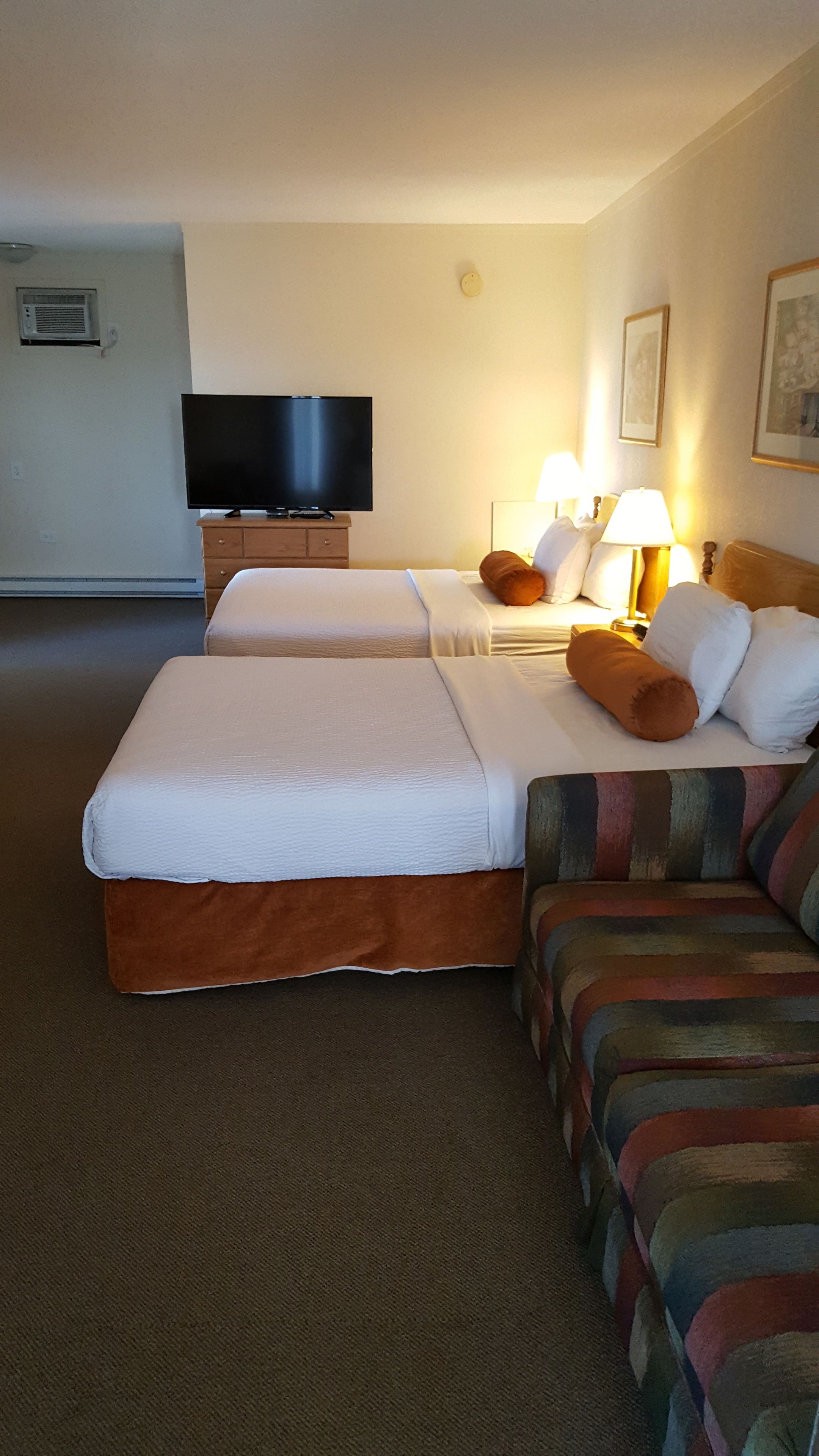 A hotel room with two beds, a television, a lamp, and a painting on the wall.