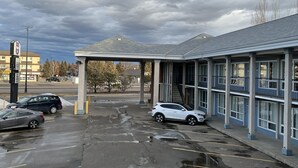 A parking lot with several cars, a building with a covered entrance, and a cloudy sky. - Knights Inn Lethbridge (Lethbridge)