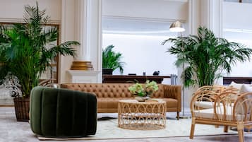 Un hall d’entrée spacieux, avec un grand canapé, une table basse ronde en osier et plusieurs plantes en pot.
