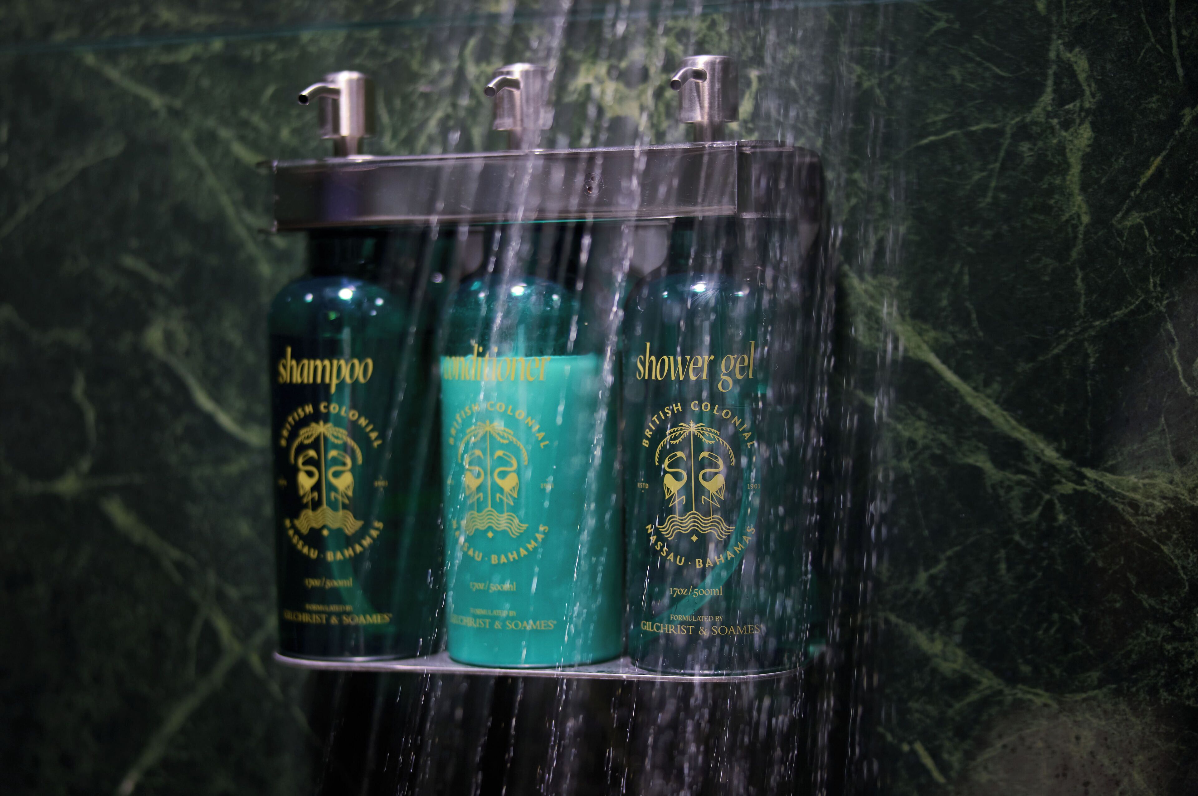 A shower area with three bottles of shampoo, conditioner, and shower gel.