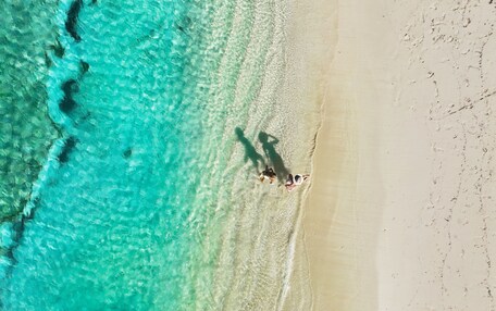 An aerial view of a beach with clear turquoise water and a sandy shore.